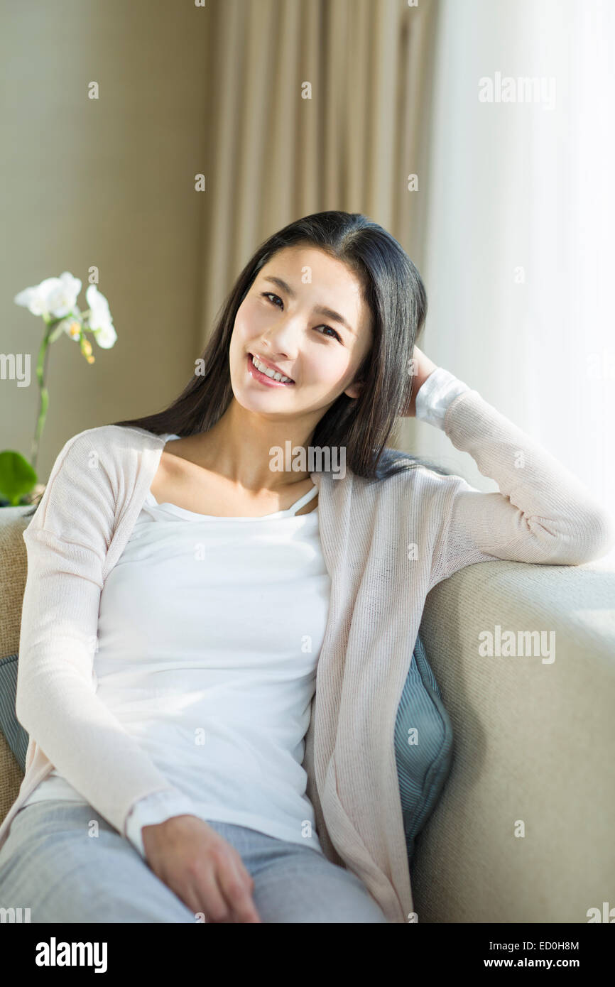 Happy young woman sitting on sofa Stock Photo - Alamy
