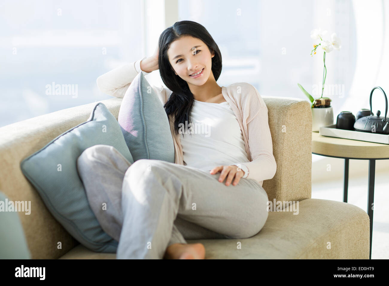 Happy young woman sitting on sofa Stock Photo - Alamy