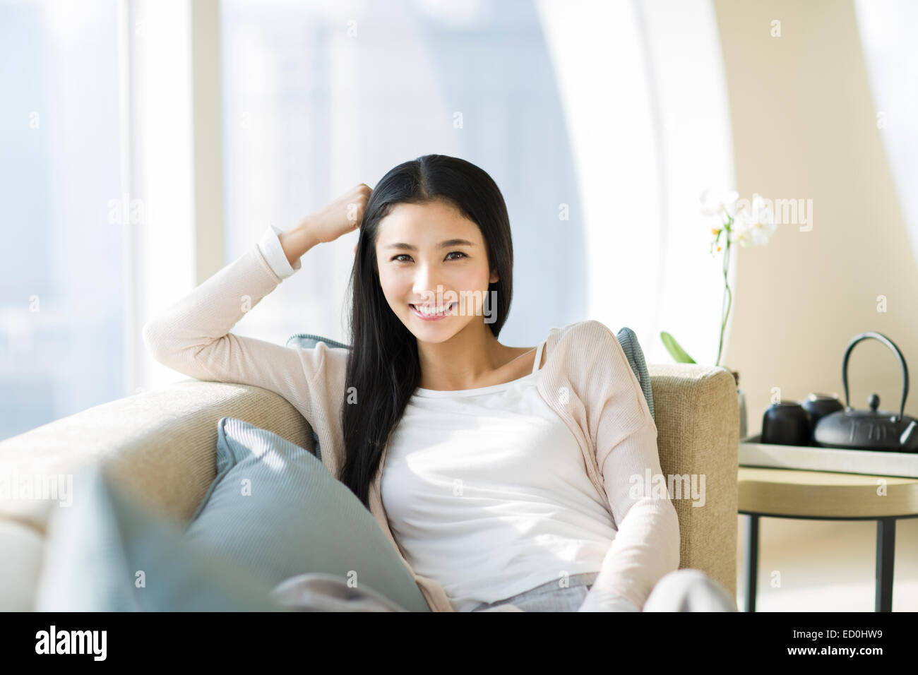 Happy young woman sitting on sofa Stock Photo - Alamy