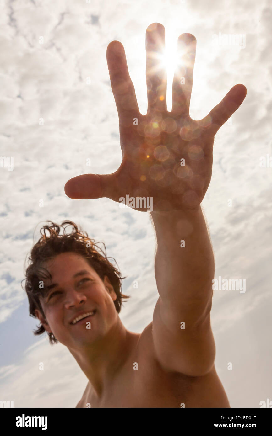 Young Asian man reaching for sun flare on vacation beach Stock Photo