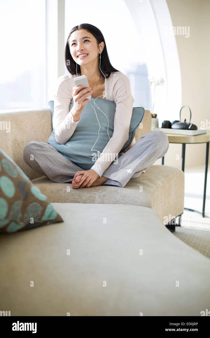 Happy young woman listening to music on sofa Stock Photo - Alamy