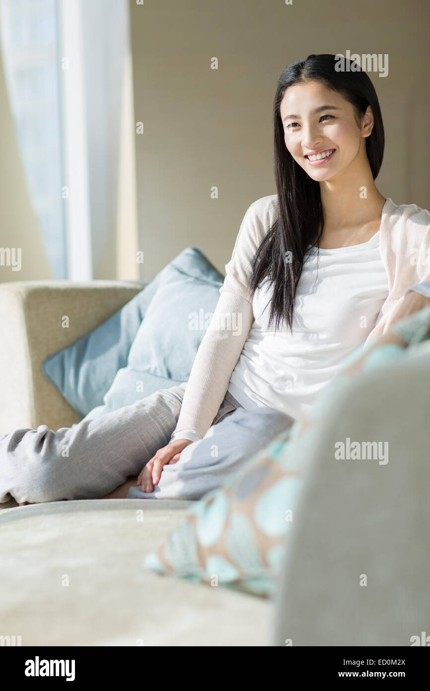 Happy young woman sitting on sofa Stock Photo - Alamy