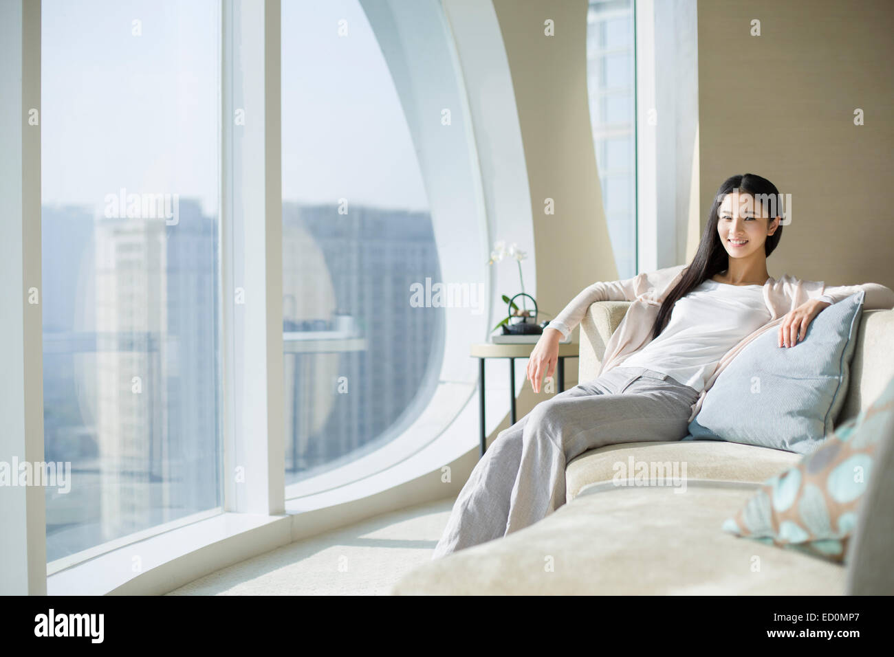 Happy young woman sitting on sofa Stock Photo - Alamy