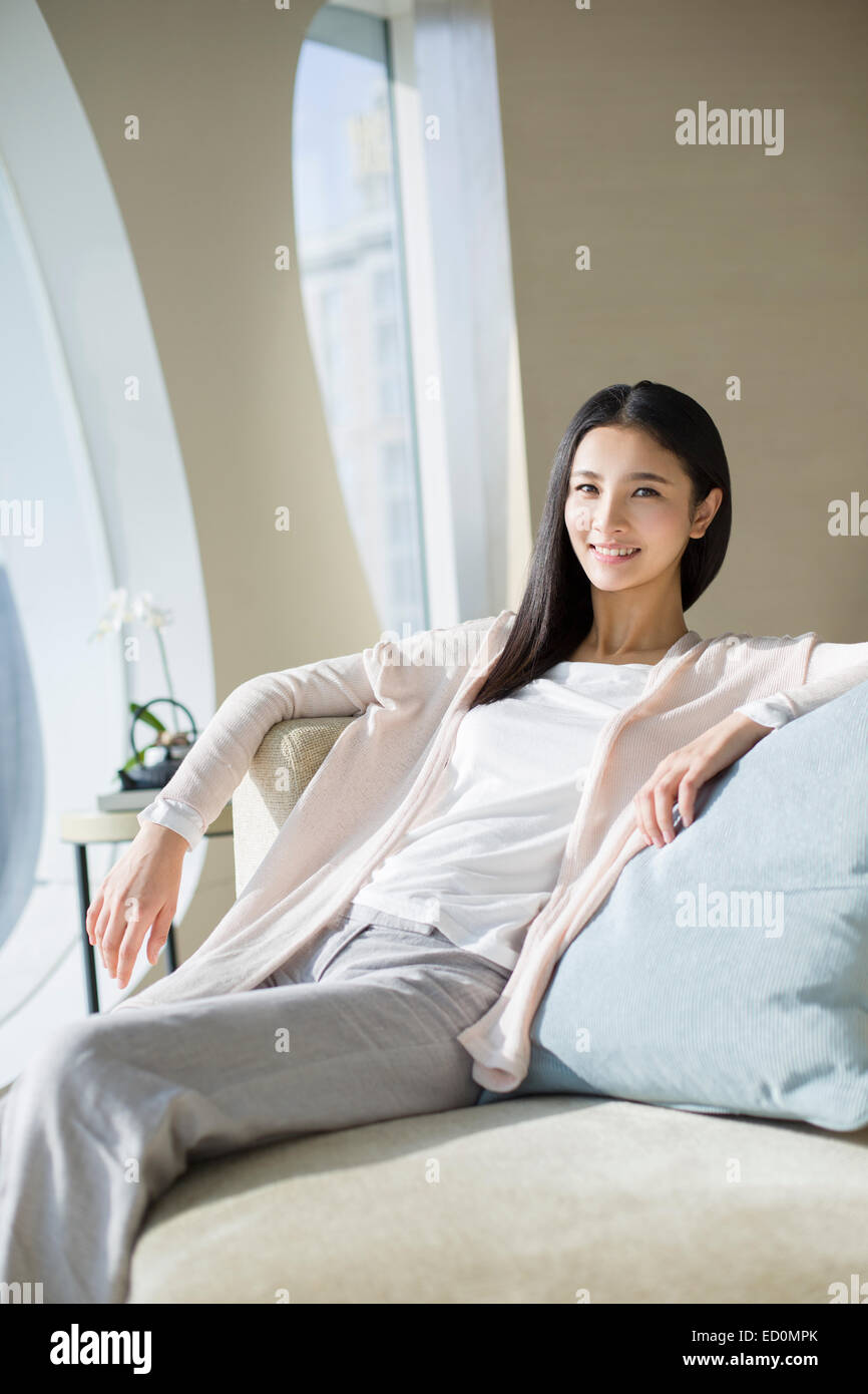 Happy young woman sitting on sofa Stock Photo - Alamy