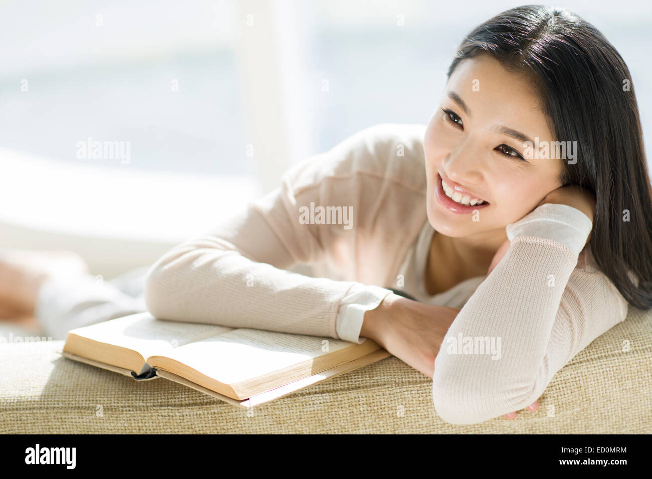 Happy young woman sitting on sofa with a book Stock Photo - Alamy