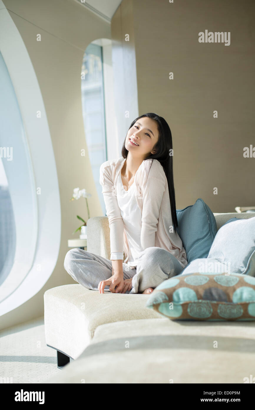 Happy young woman sitting on sofa Stock Photo - Alamy
