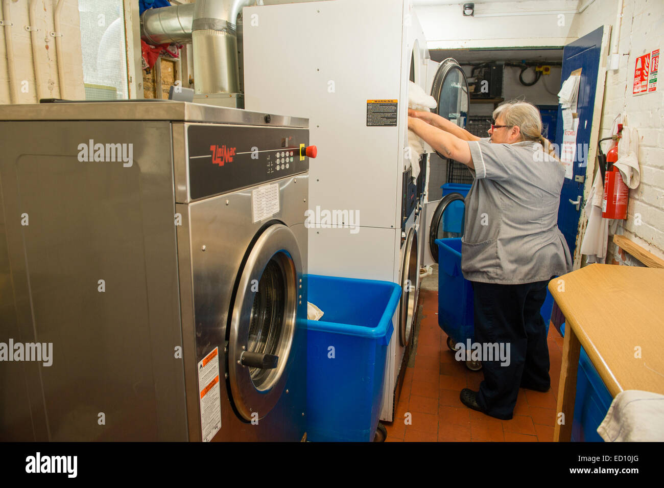 A woman working loading clothes into industrial size tumble dryers in the  laundry room at a hotel, UK Stock Photo - Alamy
