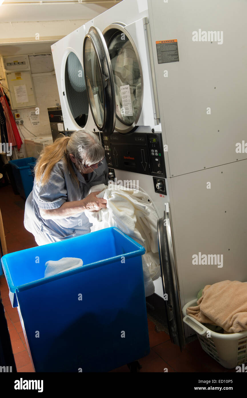 A woman working loading clothes into industrial size tumble dryers in