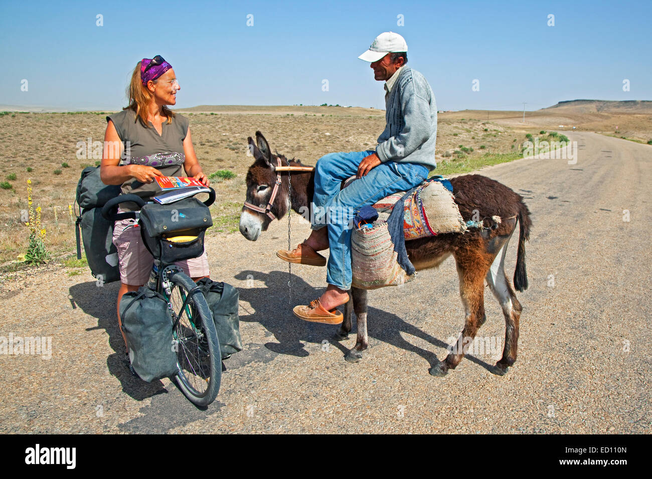 Female cyclist on touring bike asking directions to a Turkish man on donkey in Western Turkey Stock Photo