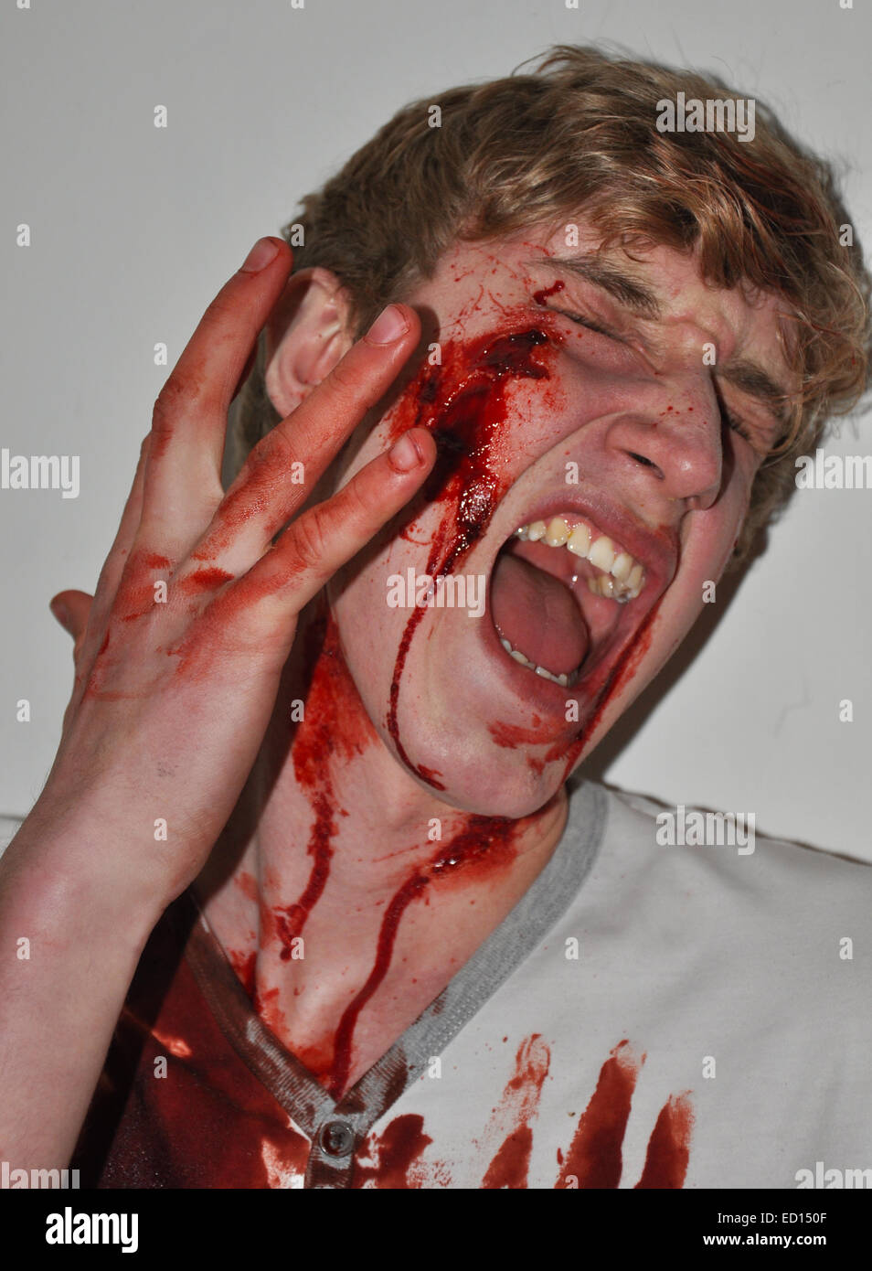 Young teenage boy screaming in pain with blood prosthetics over face Stock Photo