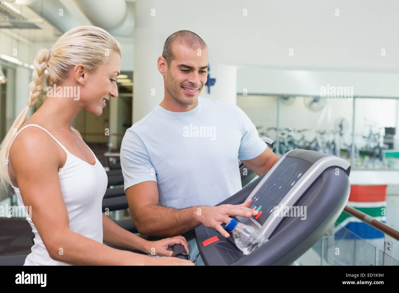 Trainer assisting woman with treadmill screen options at gym Stock ...