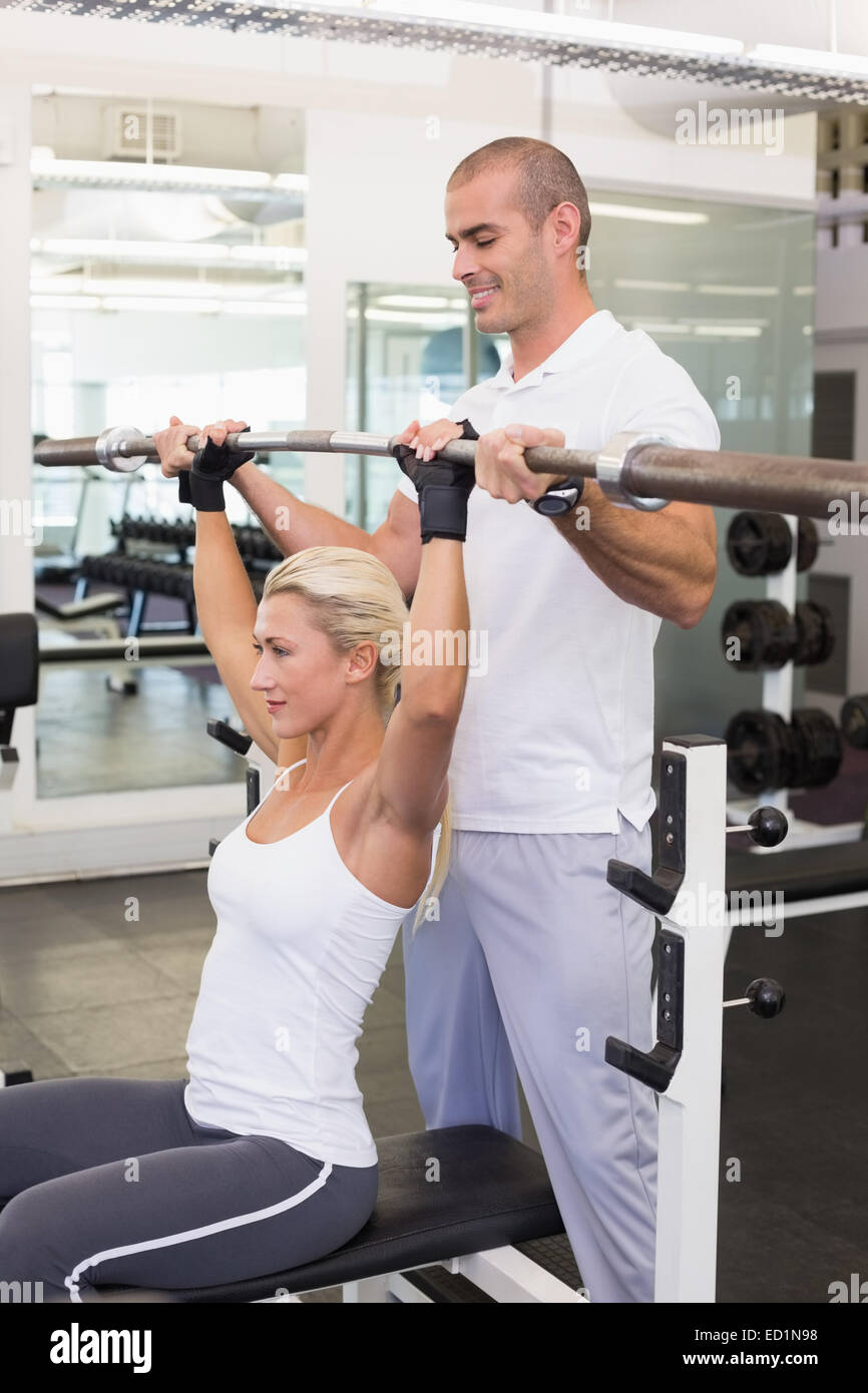 Trainer helping woman with lifting barbell in gym Stock Photo - Alamy