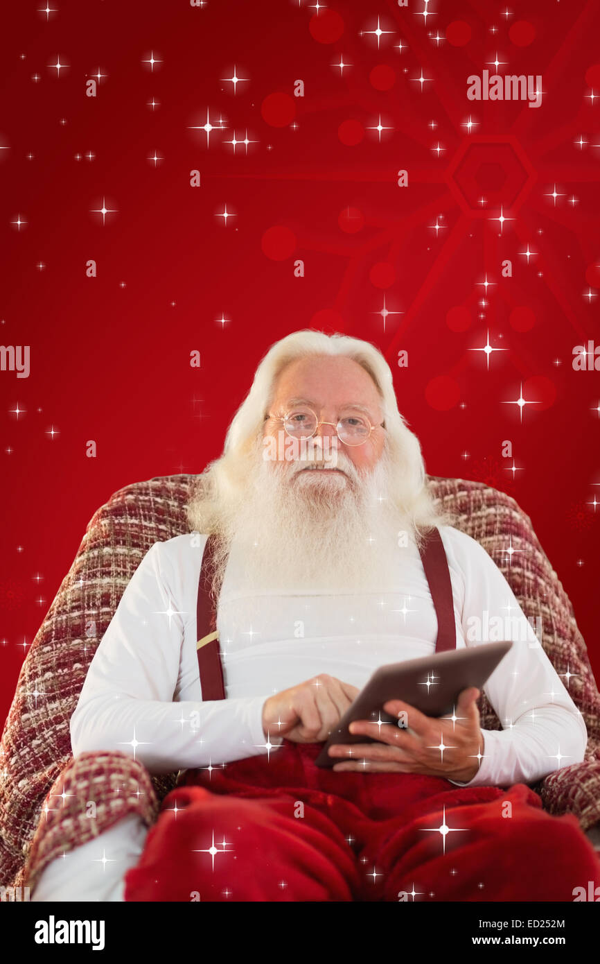Composite image of smiling santa using tablet on the armchair Stock ...