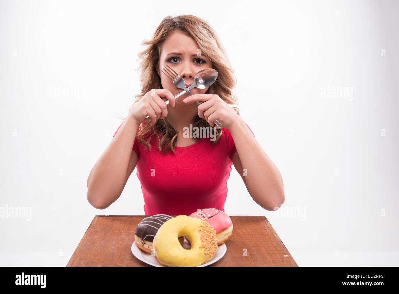 Young beautiful woman with knife and fork crossed at mouth sitti Stock