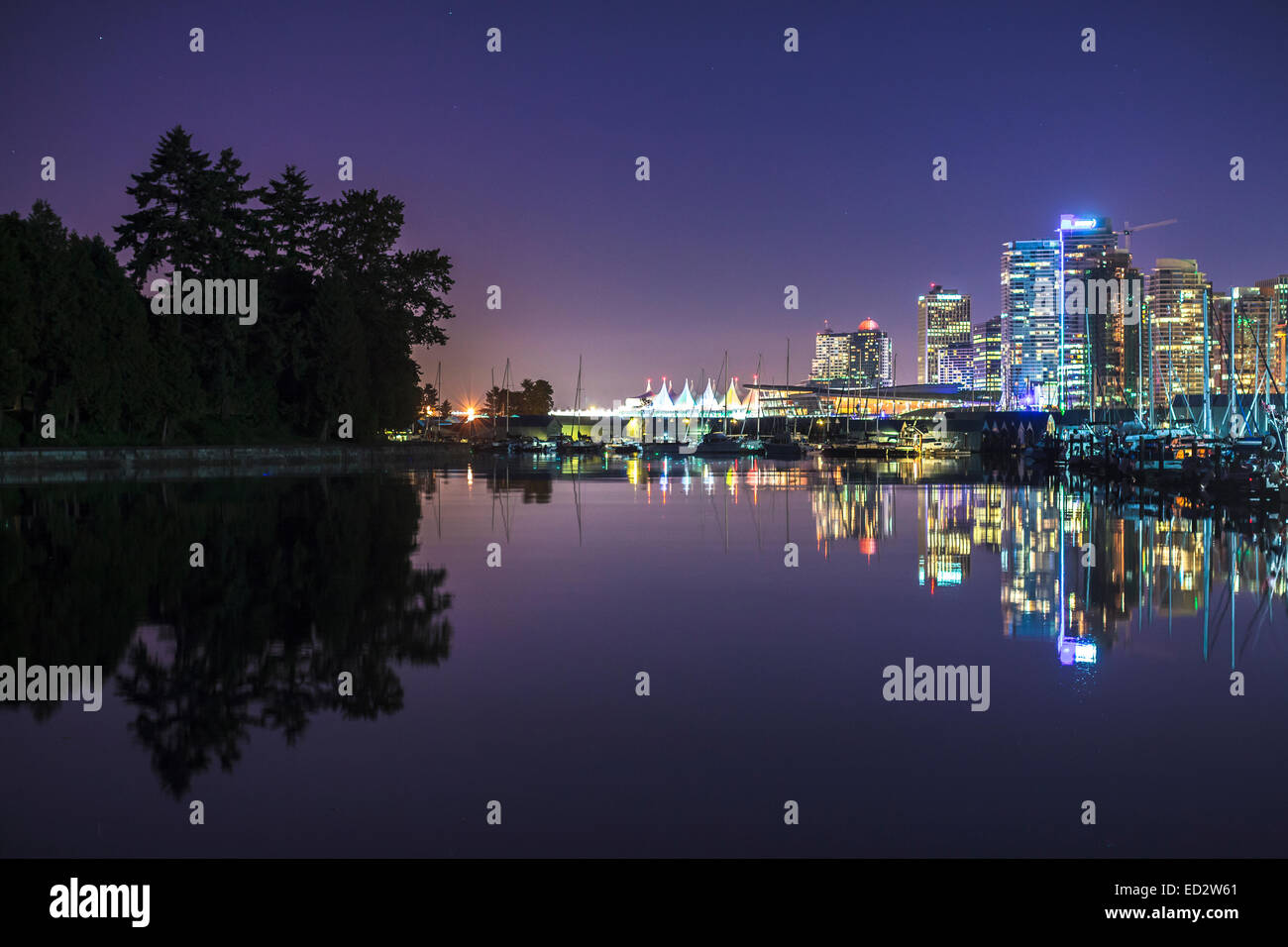 Coal harbour shimmers with the lights of apartment buildings, Canada Place, and boats in the harbour, contrasted by the towering trees of Stanley Park Stock Photo