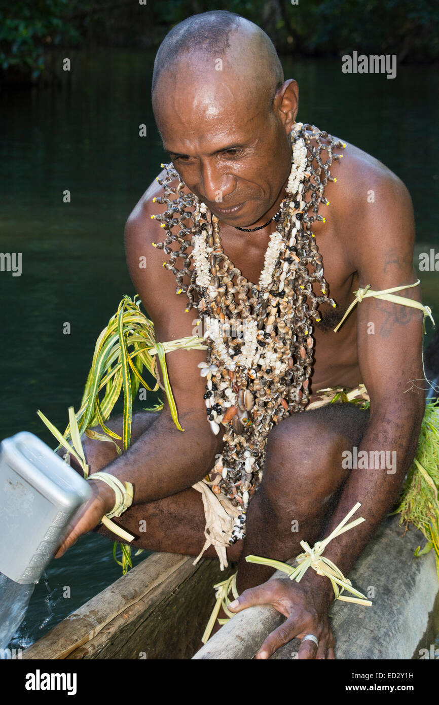 Melanesia, Papua New Guinea, Tufi. Village man in traditional attire with seashell necklaces paddling dugout canoe. Stock Photo
