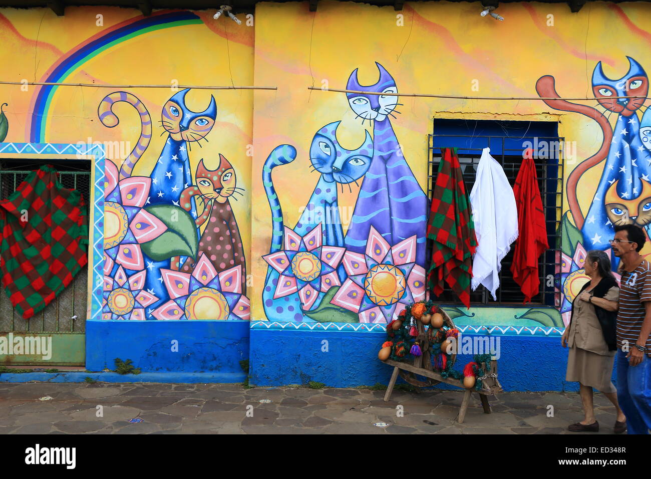 Two local people walking past a brightly coloured mural painted on the walls of a street in Ataco, Ahuachapán, El Salvador. Stock Photo