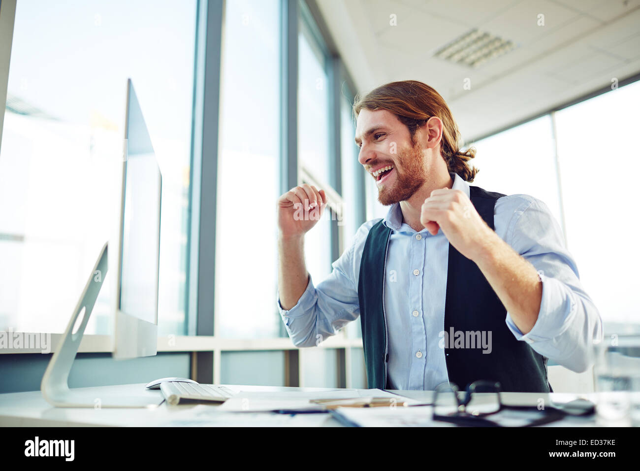Happy young employee expressing gladness while looking at monitor Stock Photo