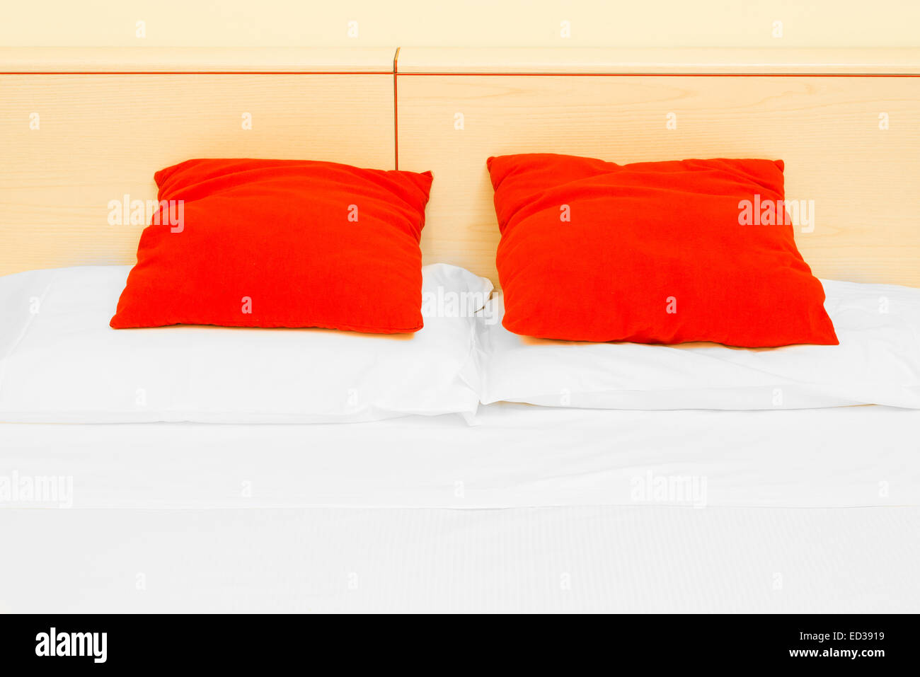 Pair of crimson cushions resting against the headboard of a bed. Stock Photo