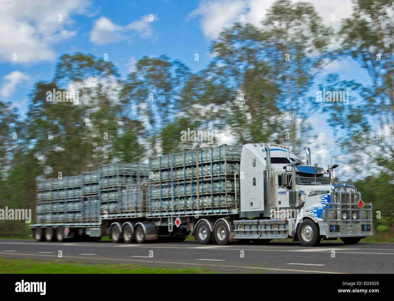 Long semi trailer truck / road train carrying dangerous cargo, cylinders of LP gas, on country road in Australia under blue sky Stock Photo
