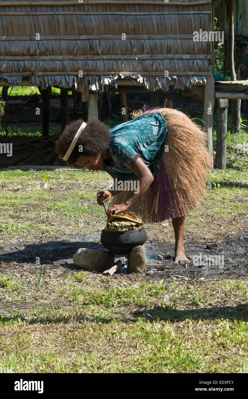 Melanesia, Papua New Guinea, Dobu Island. Village woman in grass skirt cooking with typical pottery crock over open fire. Stock Photo