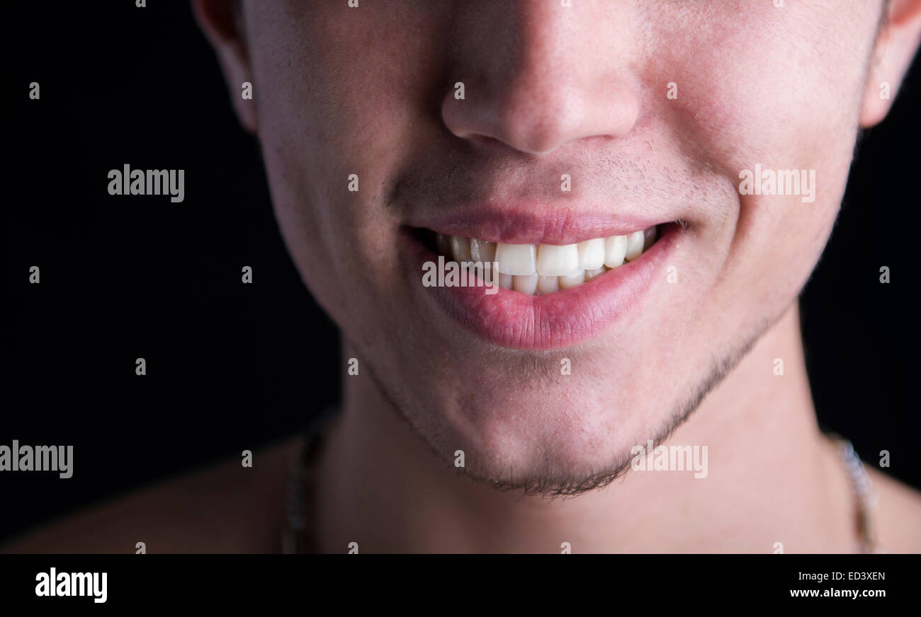Close up of white teeth and lips of a smiling young man on dark background Stock Photo