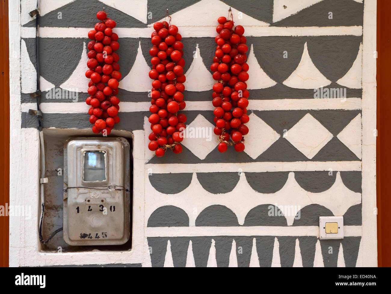 Sun-drying tomatoes hang on a wall of sgraffiti pattern, with a domestic power meter adjacent. Stock Photo