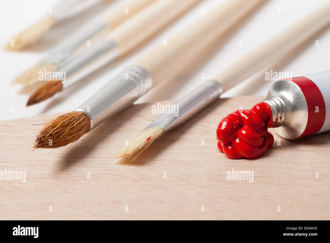 Several paintbrushes and red paint on a palette. Stock Photo