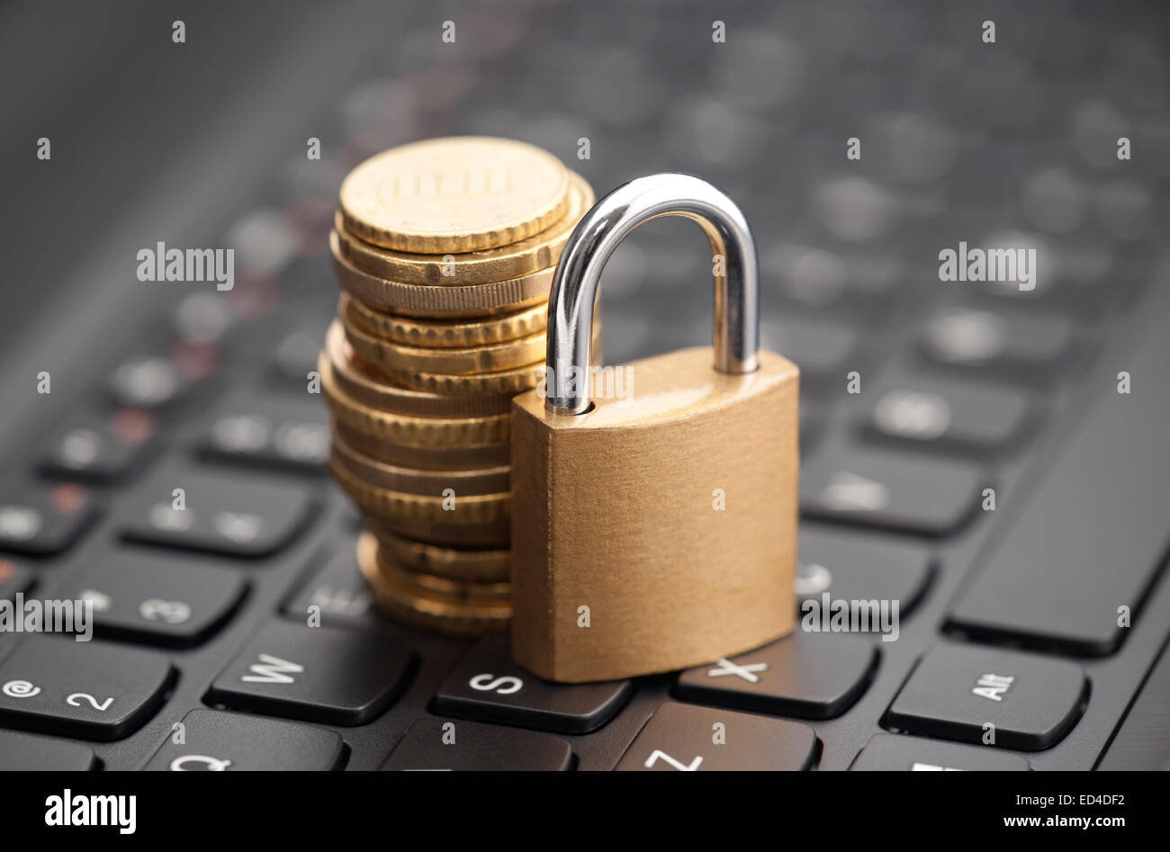 Padlock and coins on laptop keyboard Stock Photo