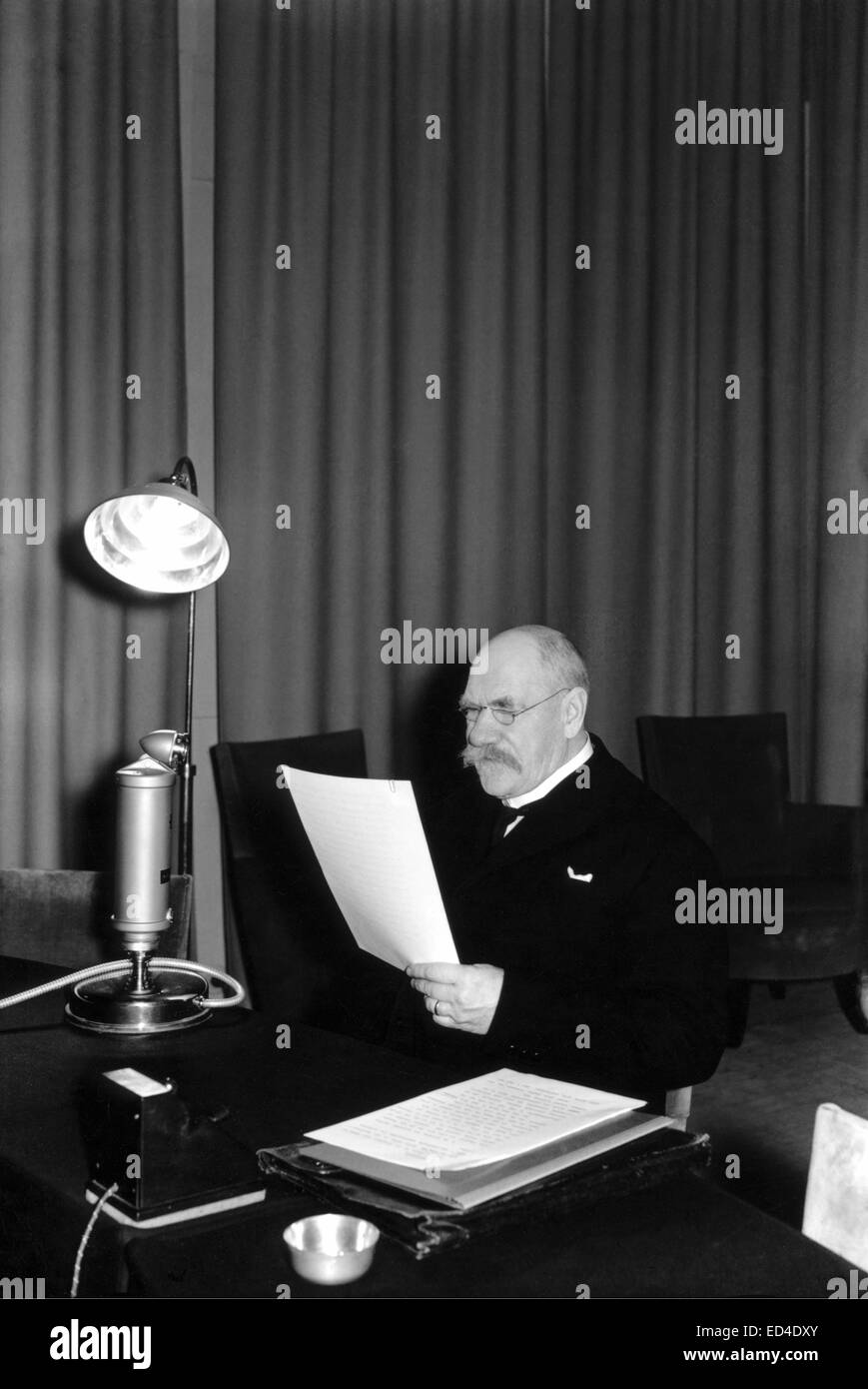 A historical photograph from the 1930s showing President Pehr Evind Svinhufvud of Finland speaking on the radio. This moment captures a significant part of Finnish political history during the interwar period. Stock Photo
