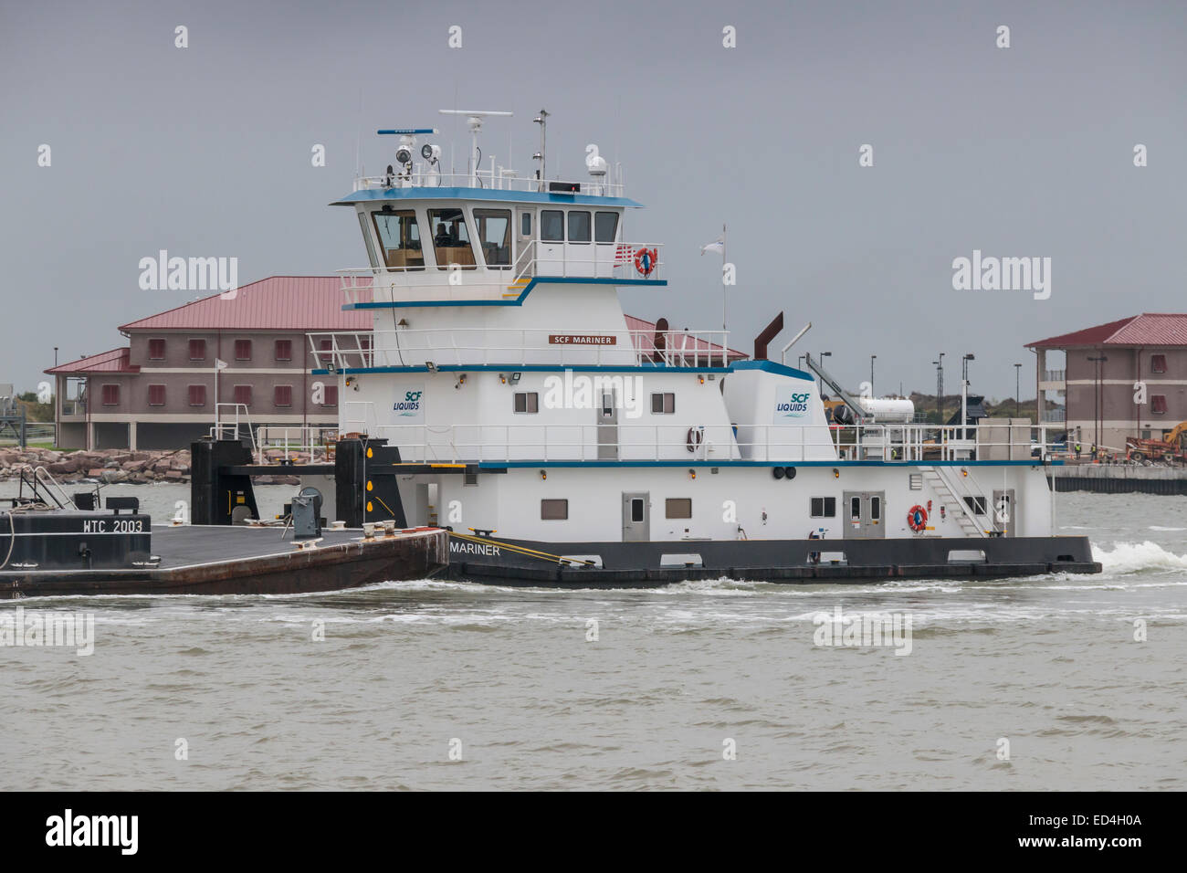 Tugboat and barge in Galveston Harbor Channel passing in front of Coast Guard station. Stock Photo