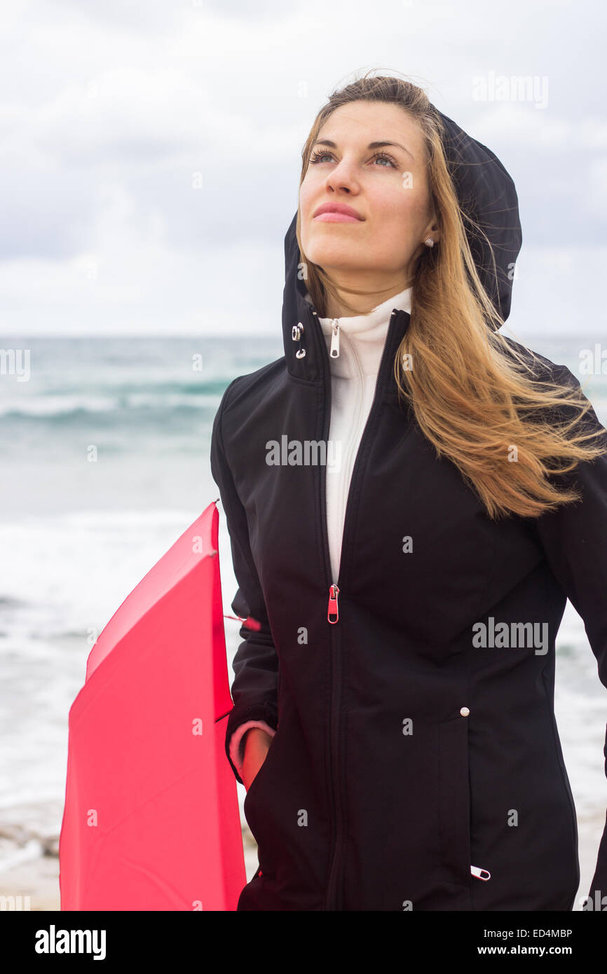 woman thoughtful dreaming red umbrella sea ocean autumn rainy day vertical portrait Stock Photo