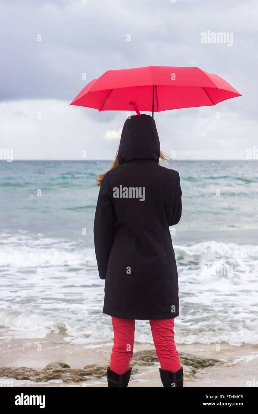woman holding red umbrella sea ocean autumn rainy day vertical back  'from behind' Stock Photo