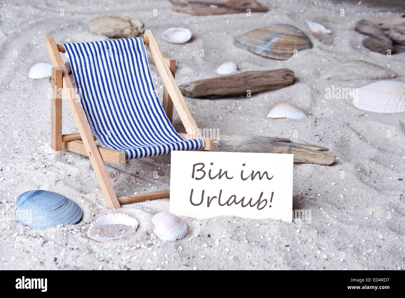 Sandy beach with deck chair and card with German text I'm on vacation