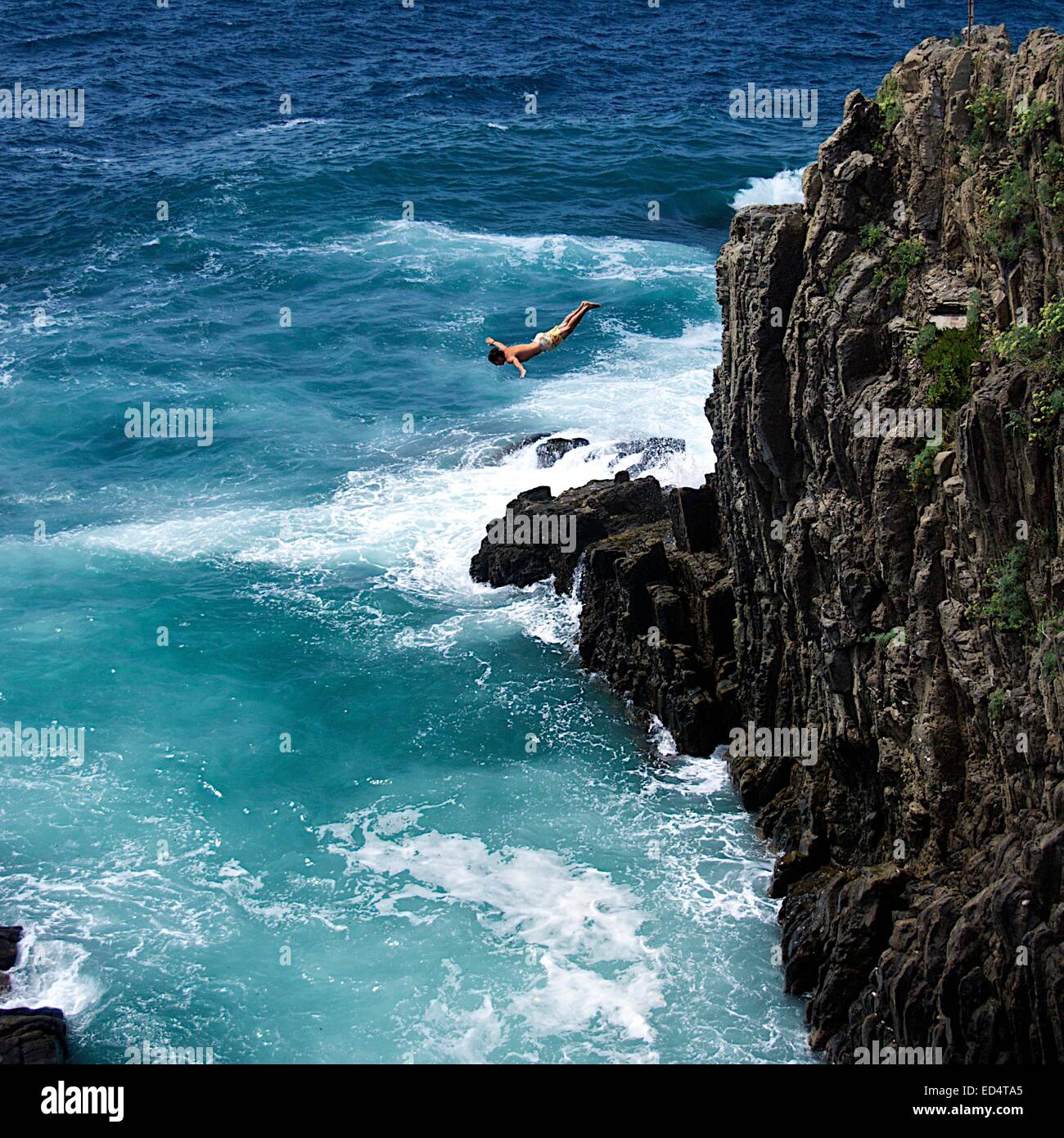 Man diving from rocky cliff into the ocean in Manarola on the Cinque Terre, Northern Italy Stock