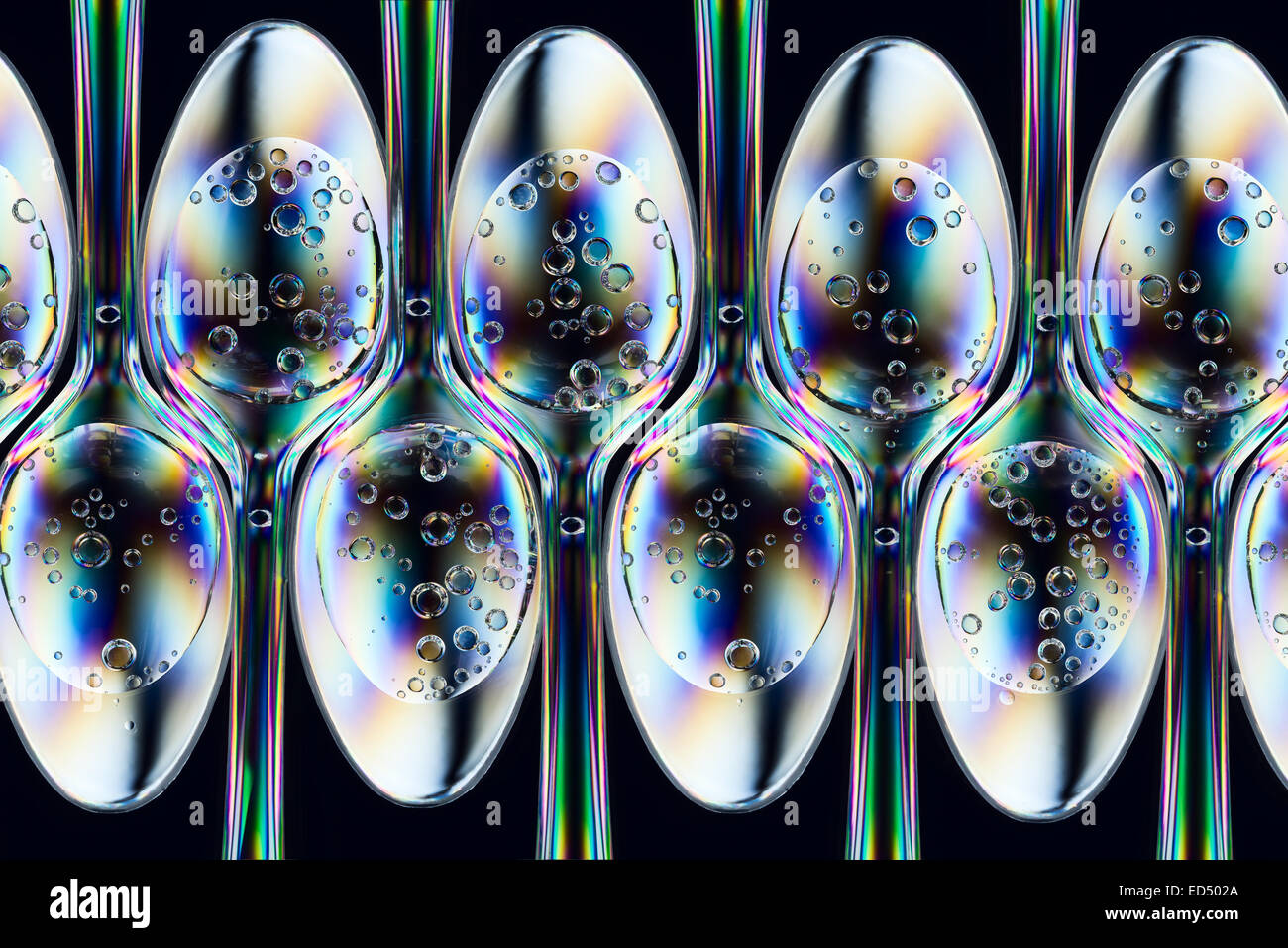 Polarized stress patterns in row of plastic spoons with carbonated liquids from above     Stock Photo