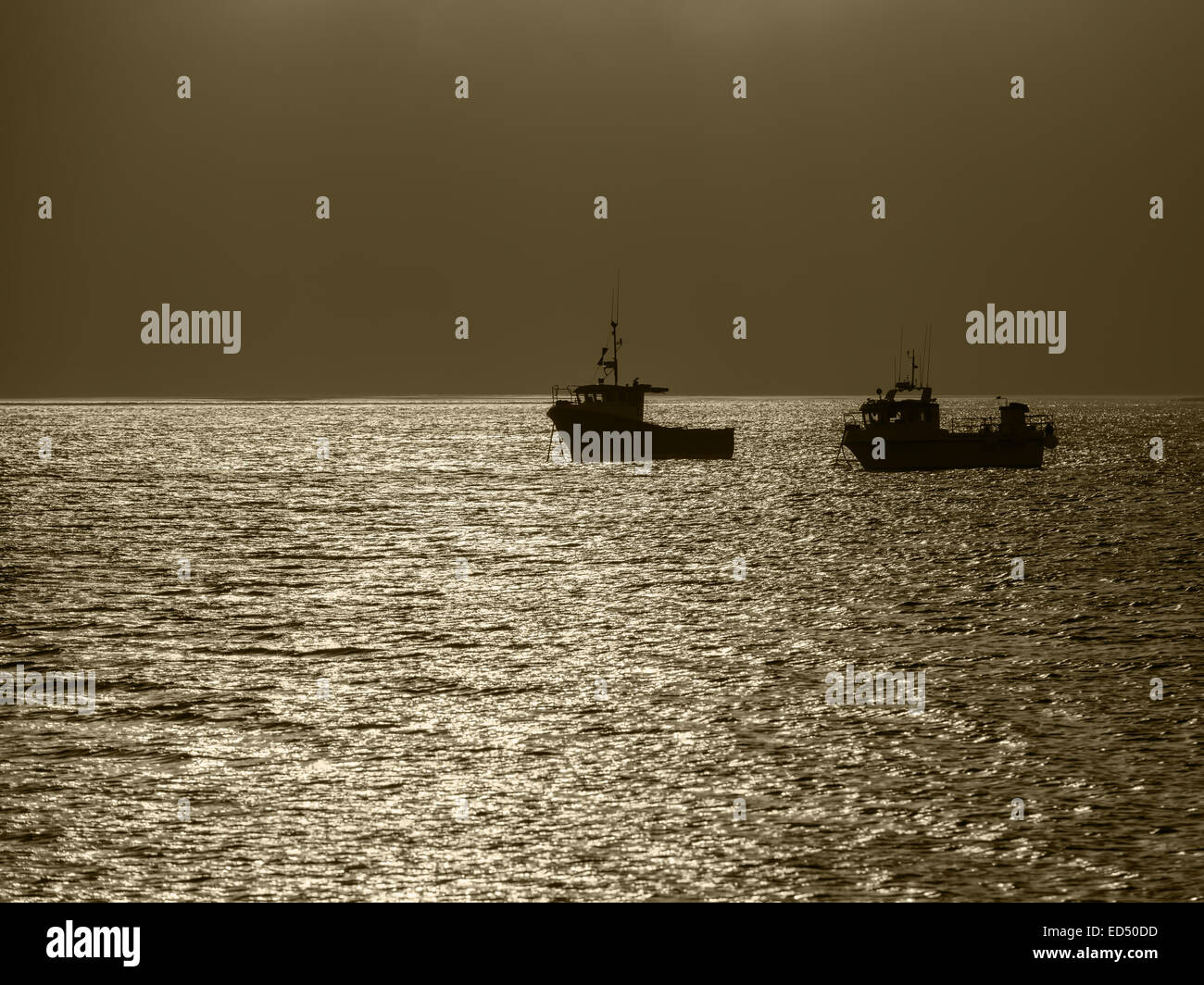 Two fishing boats moored off Holy Island, Northumberland, England. They are silhouetted against the sunlight. The boats are in Holy Island Harbour. Stock Photo