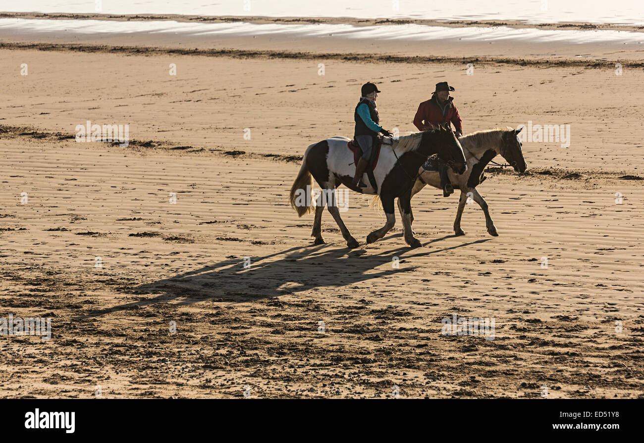 Horse riders casting shadows on the beach at Merthyr Mawr, Wales, UK Stock Photo