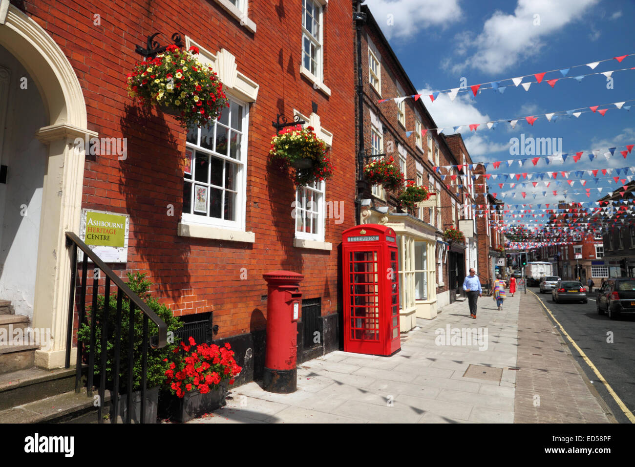 A street of an English town with red brick buildings, bunting, a red telephone box, and a pillar box. Stock Photo