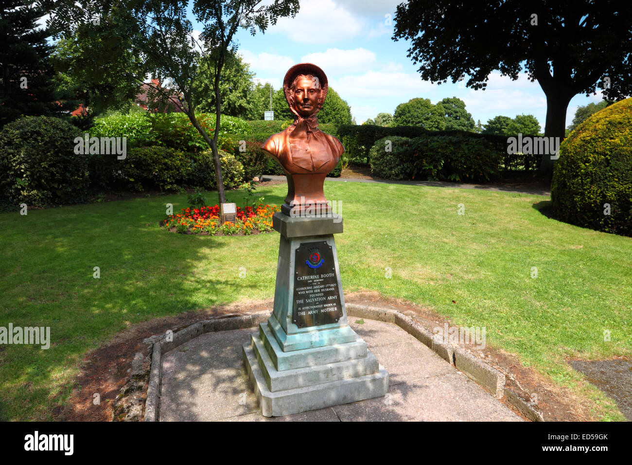 A copper bust of a lady wearing a bonnet on a plinth in a park amongst trees. Stock Photo