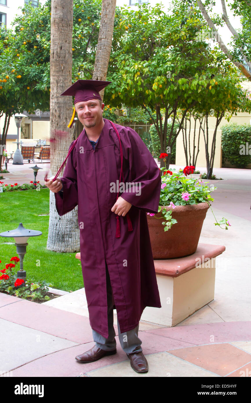 Mature college graduate in cap and gown happily twirling tassels Stock Photo