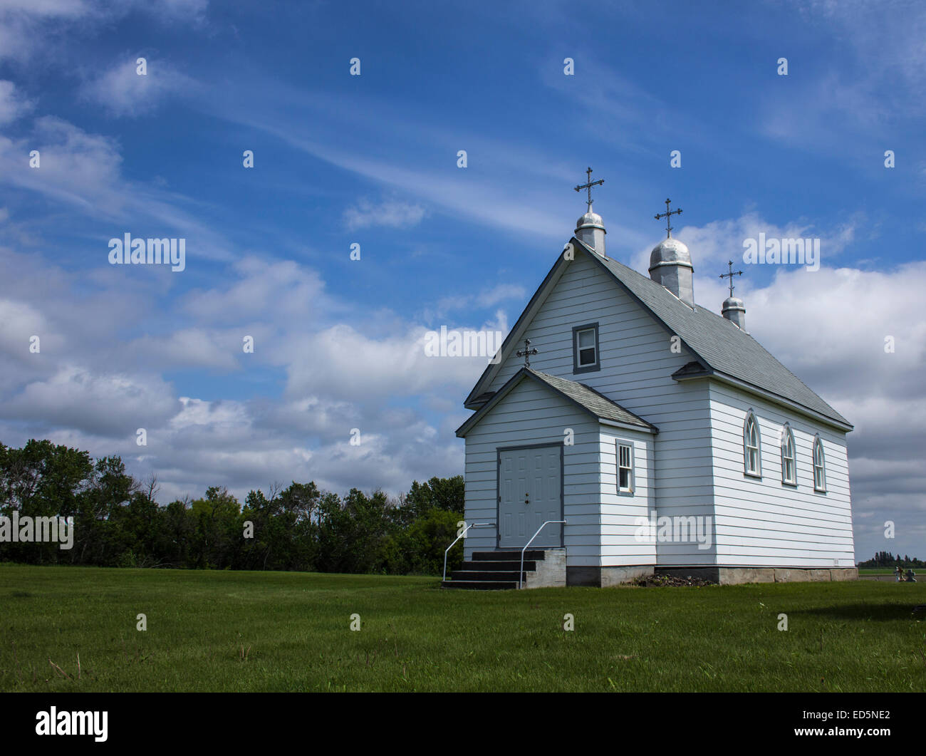 Little white country church with three steeples and crosses on the Prairie on a clear summer day with green grassy field. Stock Photo