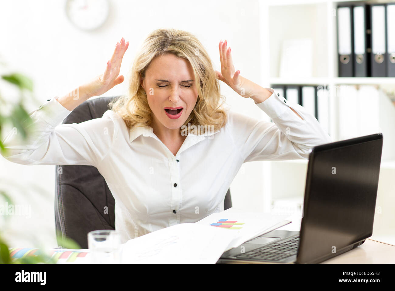 Stressed businesswoman screaming loudly at laptop in office Stock Photo