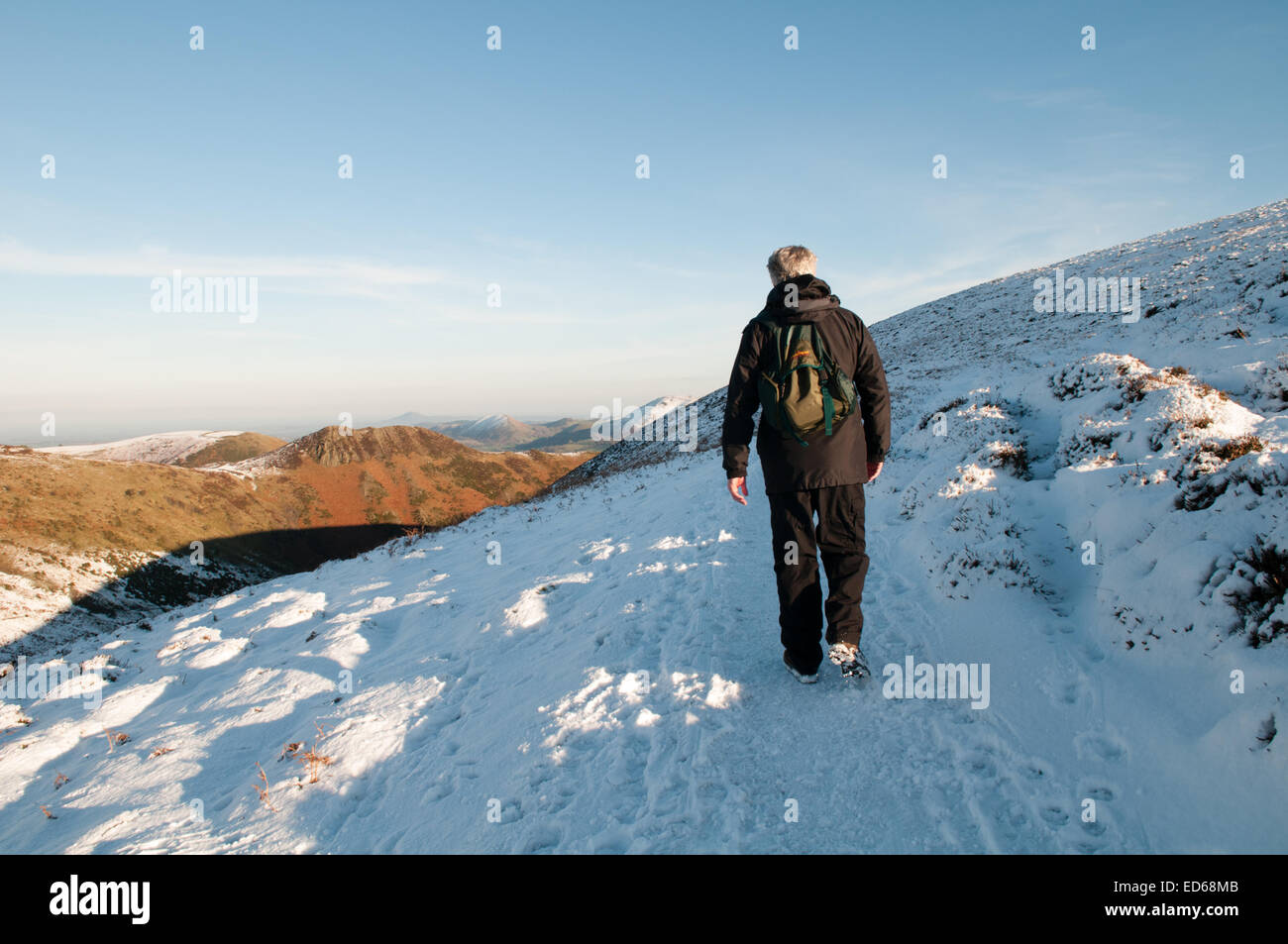 Long Mynd, Shropshire, UK. 29th December, 2014. Weather UK: Glorious winter sunshine bathes the UK giving walkers wonderful winter treks over snow-covered hills as temperatures drop below freezing as 2014 comes to an end. Here a man is walking along a snow-covered and stunning Long Mynd, in Shropshire, looking out across the snow-capped hills on a wonderful winter's day walk. Credit:  Jane Williams/Alamy Live News Stock Photo