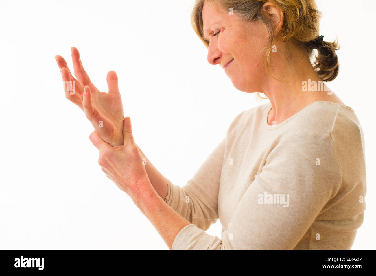 A forty year old caucasian woman with painful arthritis in the joints of her hand wrist and fingers, rubbing her wrist for pain relief, against a white background. UK Stock Photo