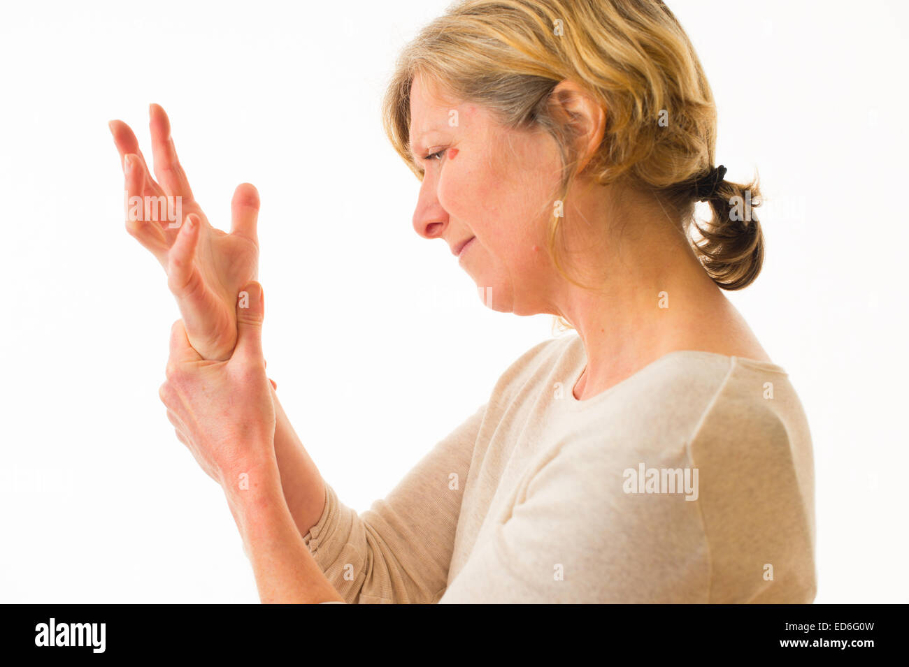 A forty year old caucasian woman with painful arthritis in the joints of her hand wrist and fingers, rubbing her wrist for pain relief, against a white background. UK Stock Photo