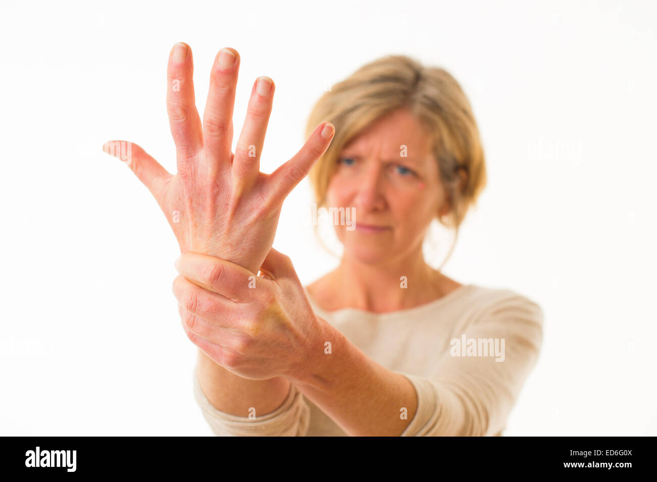 A forty year old caucasian woman with painful arthritis in the joints of her hand wrist and fingers, rubbing her wrist for pain relief, against a white background. UK Stock Photo