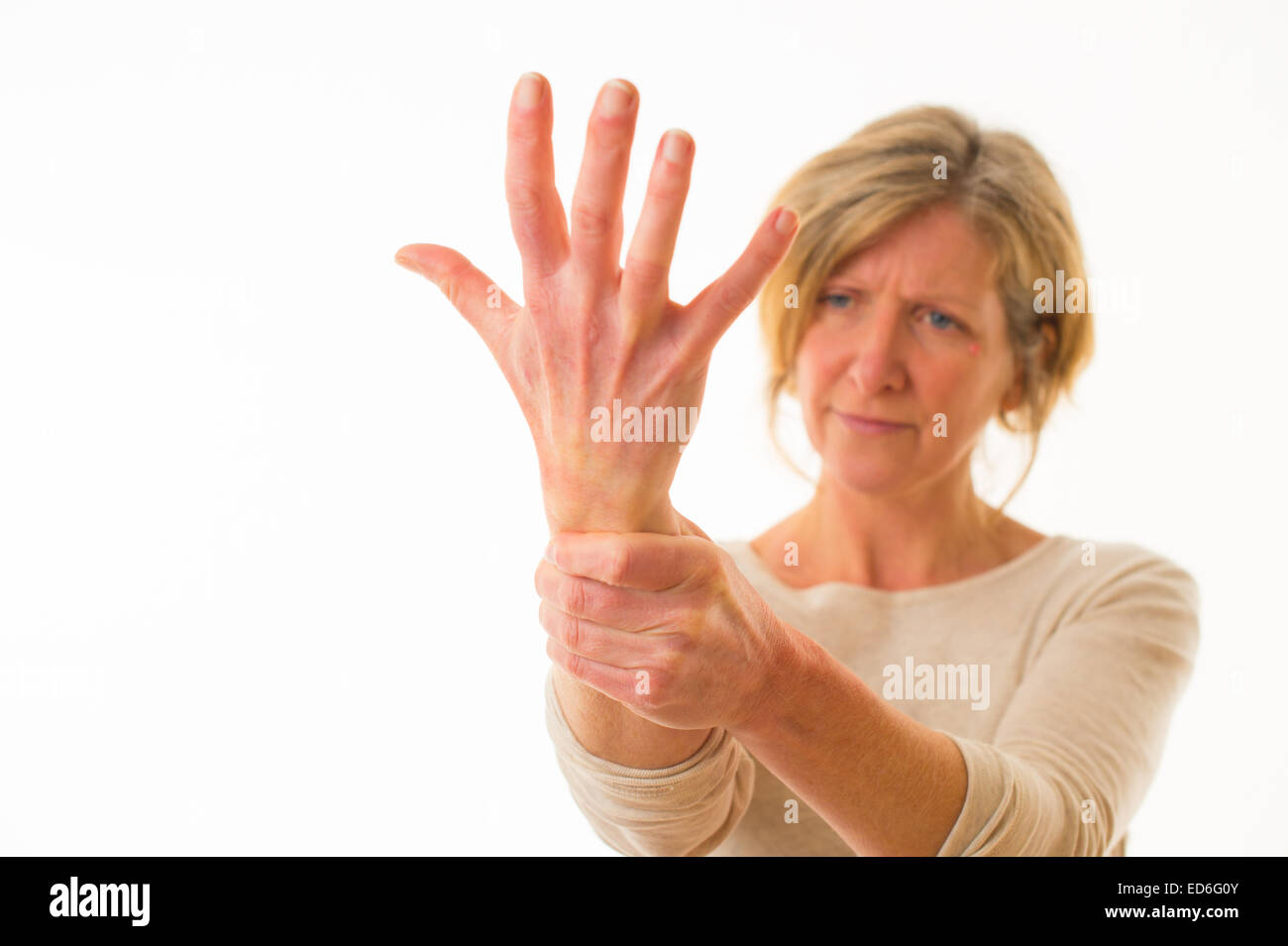 A forty year old caucasian woman with painful arthritis in the joints of her hand wrist and fingers, rubbing her wrist for pain relief, against a white background. UK Stock Photo