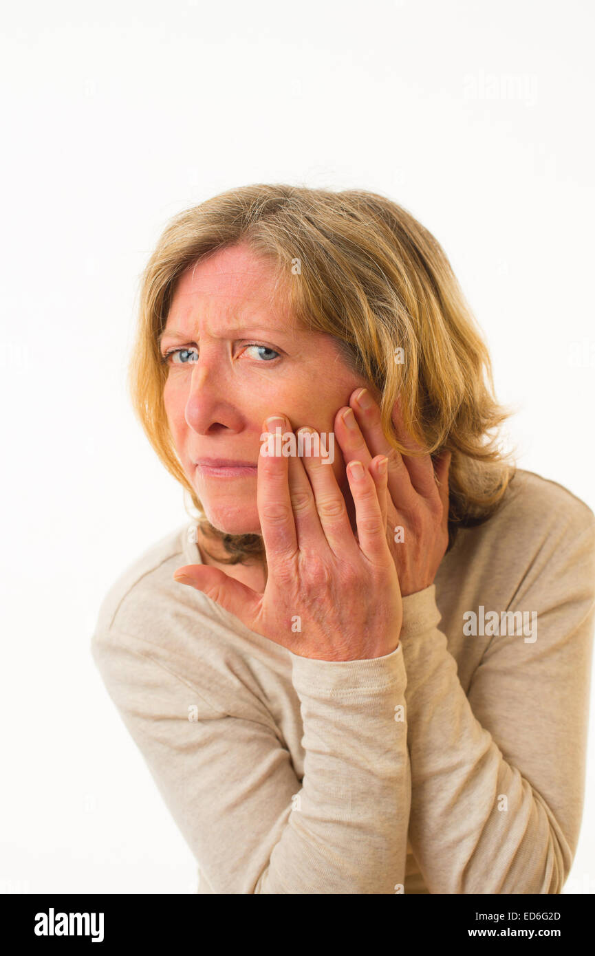 Health worry: A forty year old adult concerned worried anxious caucasian woman checking her face skin complexion against a white background. UK Stock Photo