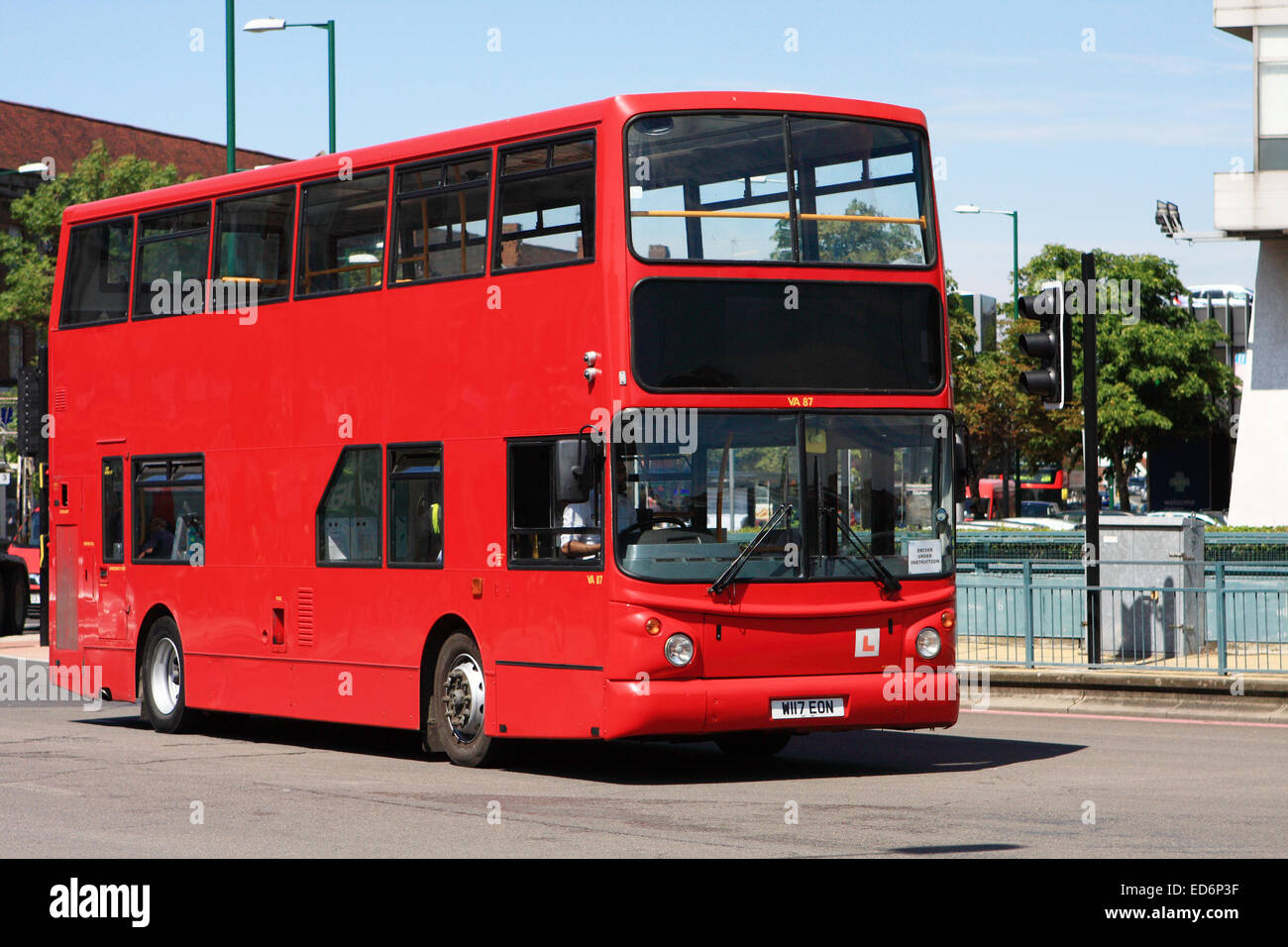 A learner driver driving a double decker red London bus onto a